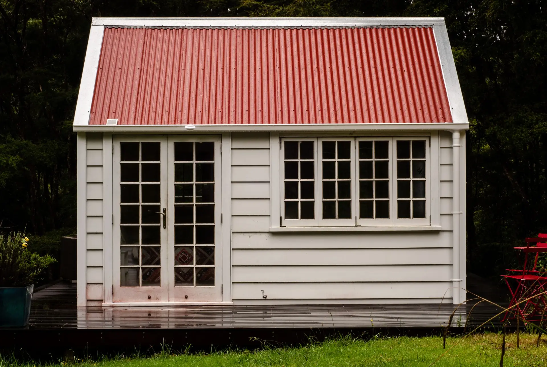 Small white cottage with a red metal roof and glazed doors