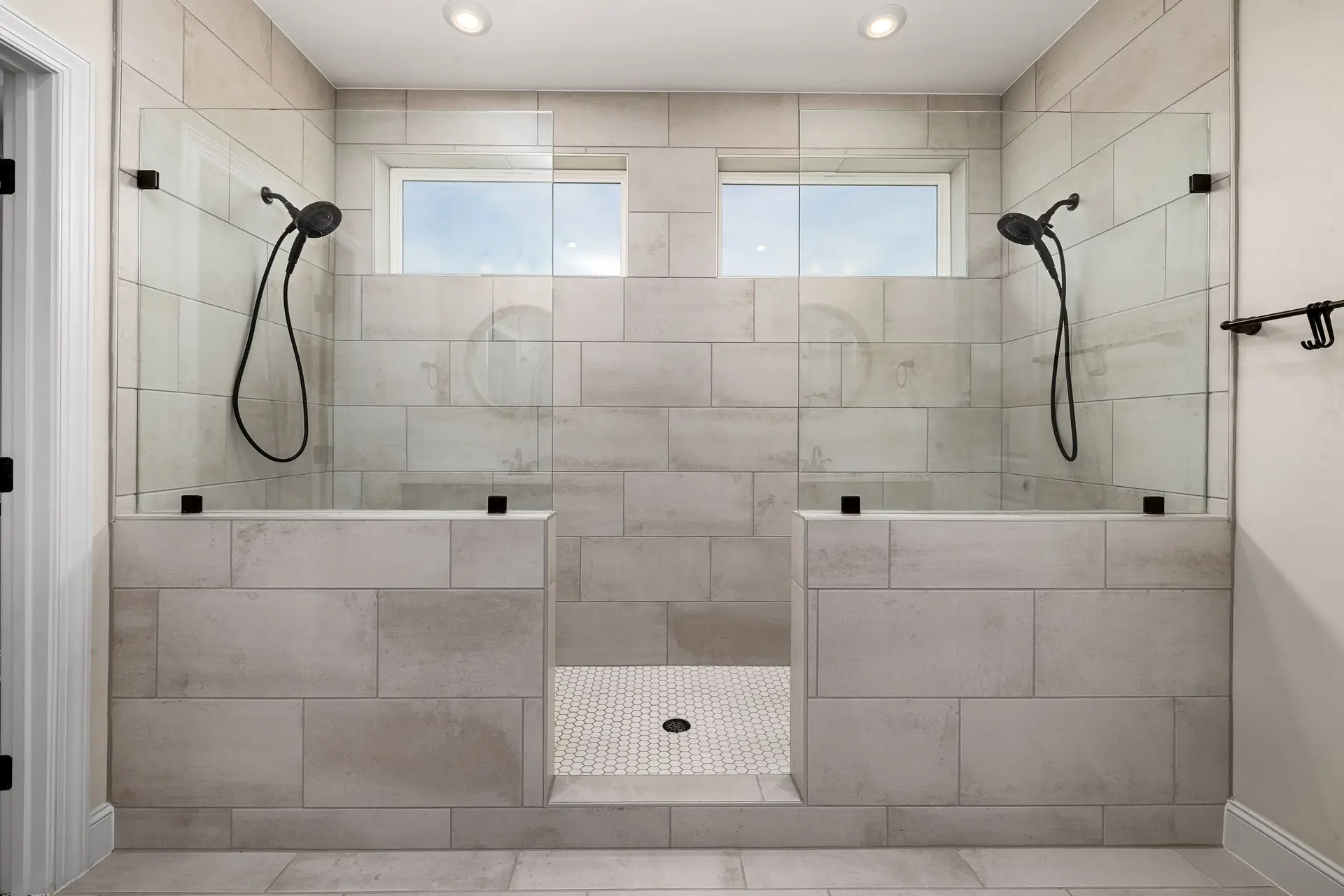 Double walk-in shower in large gray tile below two windows